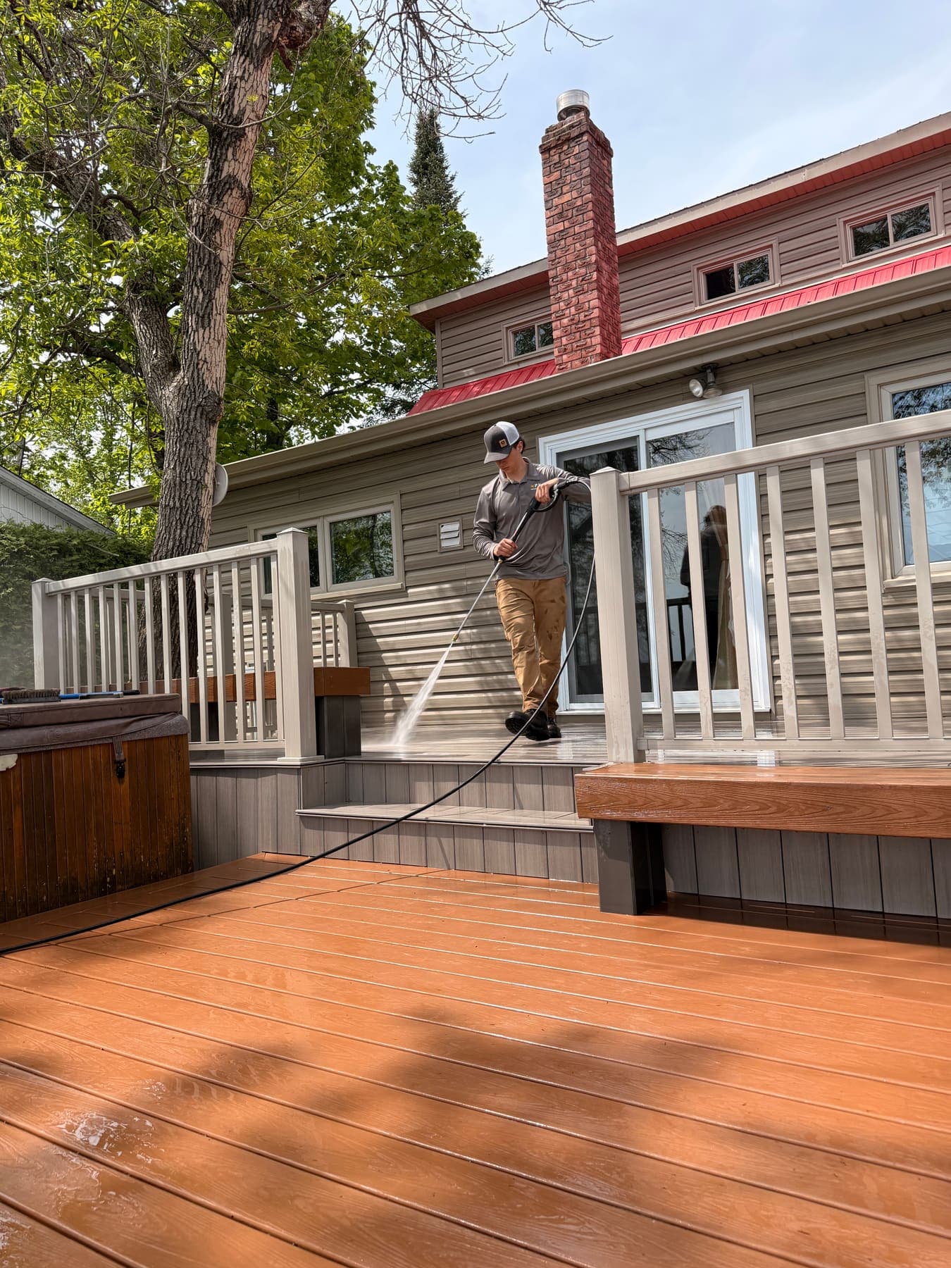 Crew member pressure-washing the underside of a porch with white railings, warm wood deck visible.