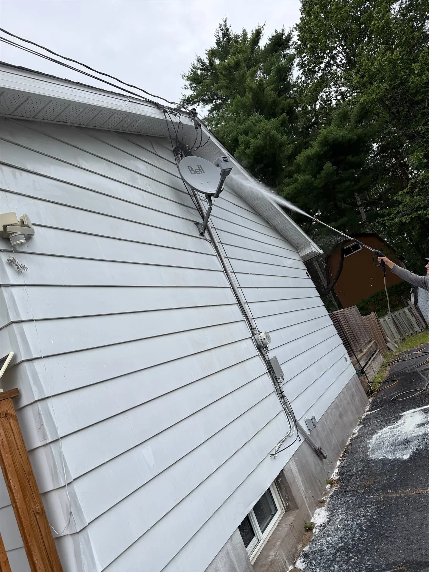 Pressure wand rinsing soffit and eaves on a white-sided home in the Ottawa Valley