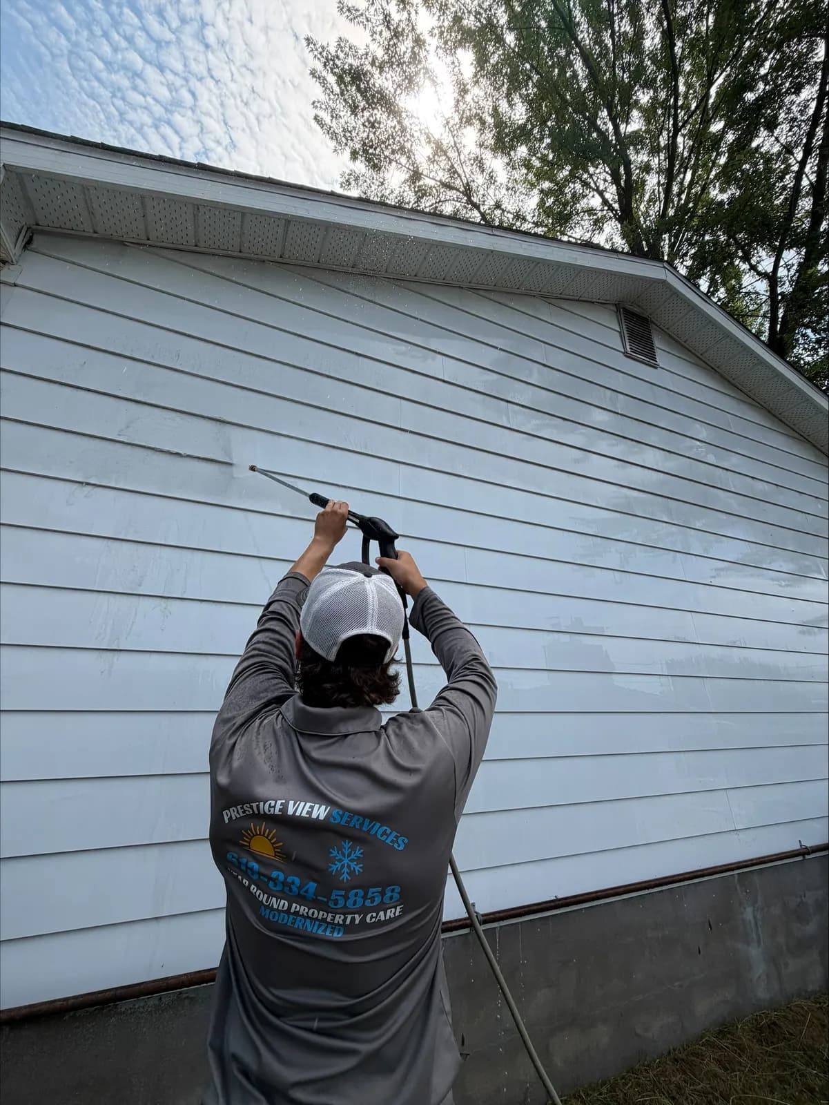 PVS crew member in branded shirt soft-washing white siding of a Petawawa home