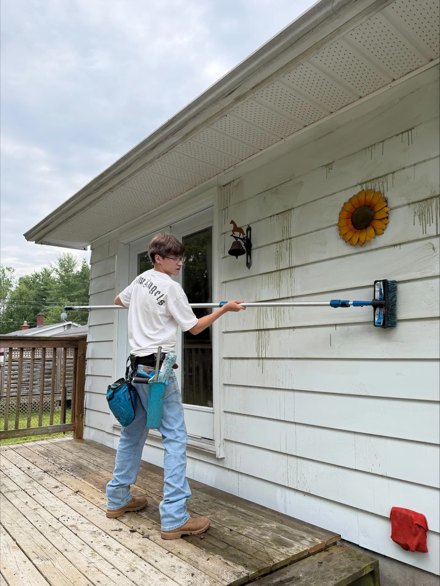 Crew member scrubbing white siding with an extension brush, soap suds running down the wall