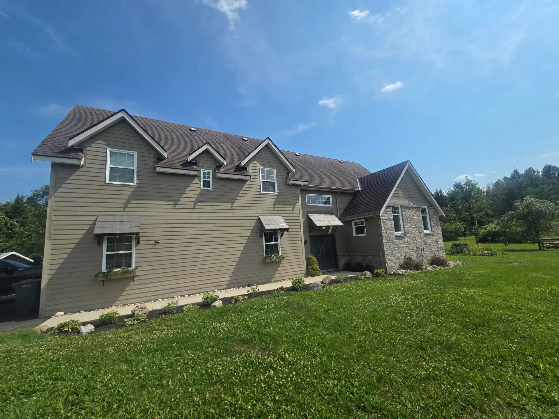 Beige two-storey home with manicured lawn and landscaped beds under blue sky near Pembroke