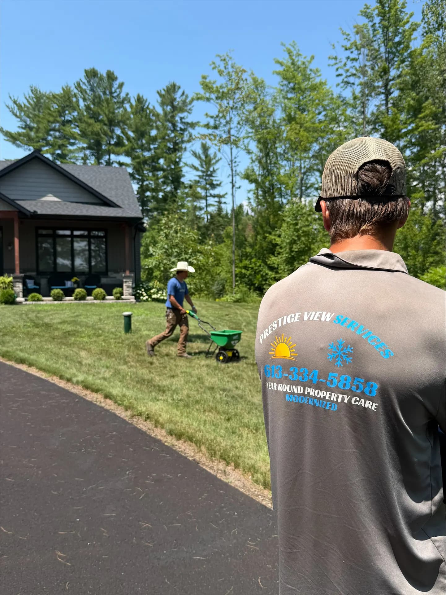 PVS lawn care crew in branded shirts running a fertilizer spreader at a modern Petawawa home