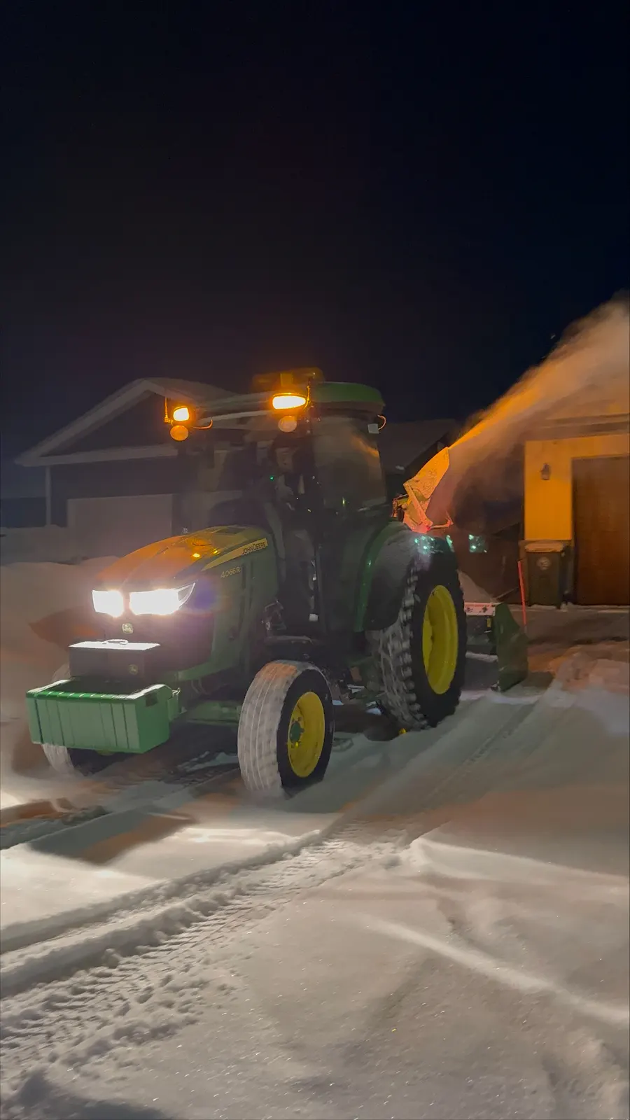 John Deere tractor snow-blowing a driveway at night with headlights on in Pembroke