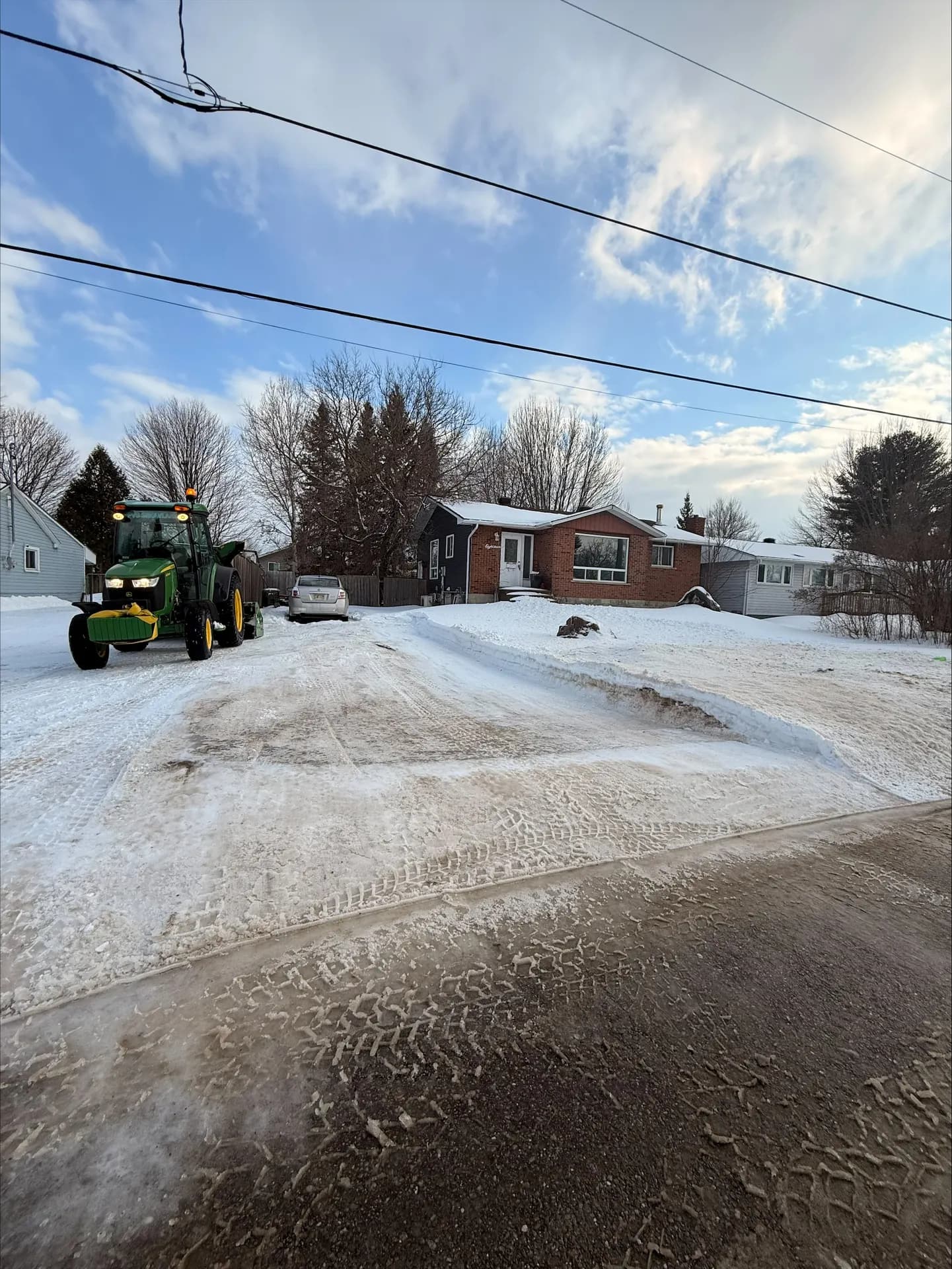 Tractor with front blade clearing a residential driveway under a blue winter sky in the Ottawa Valley