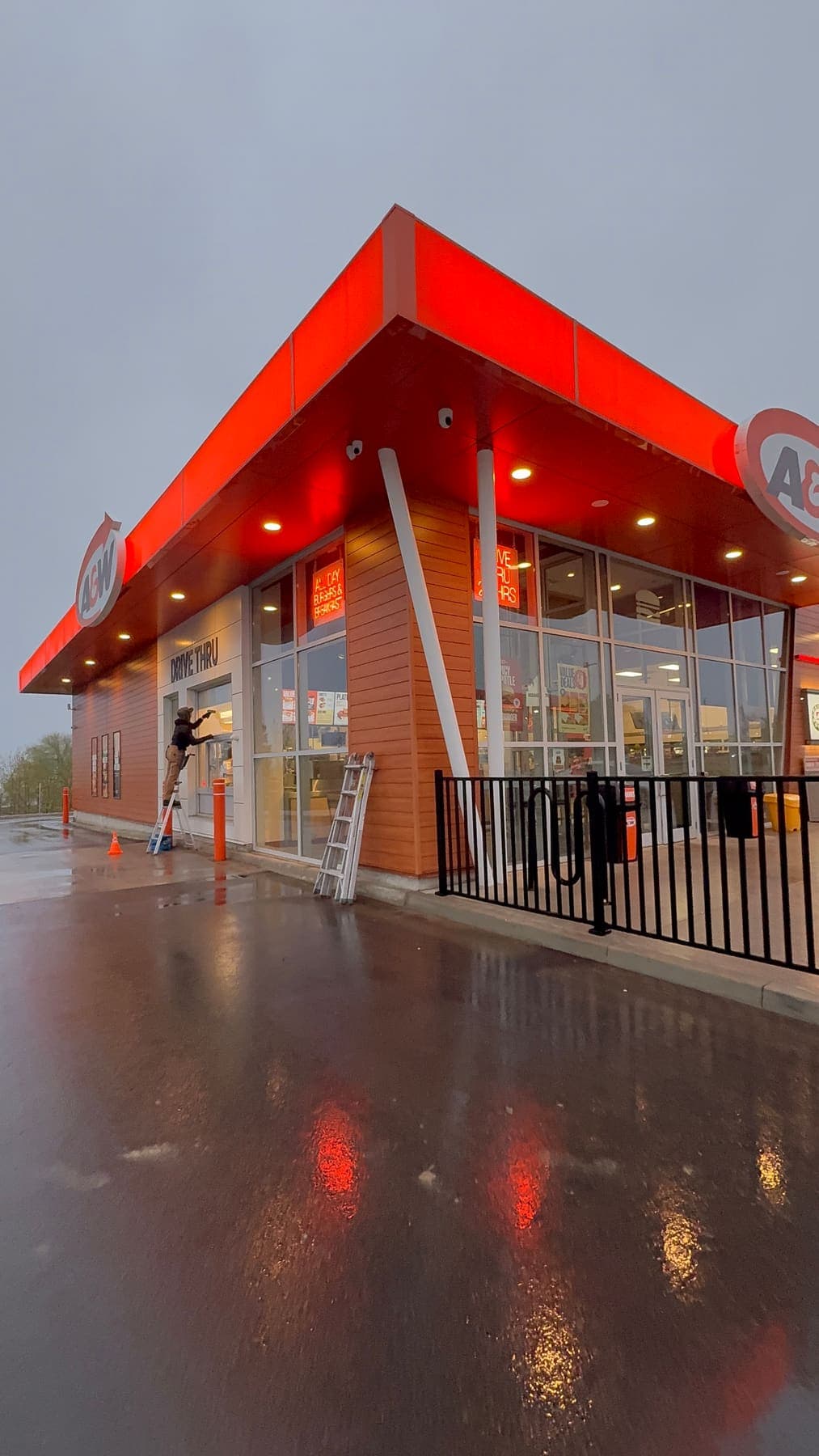 PVS technician cleaning A&W storefront windows on a rainy day