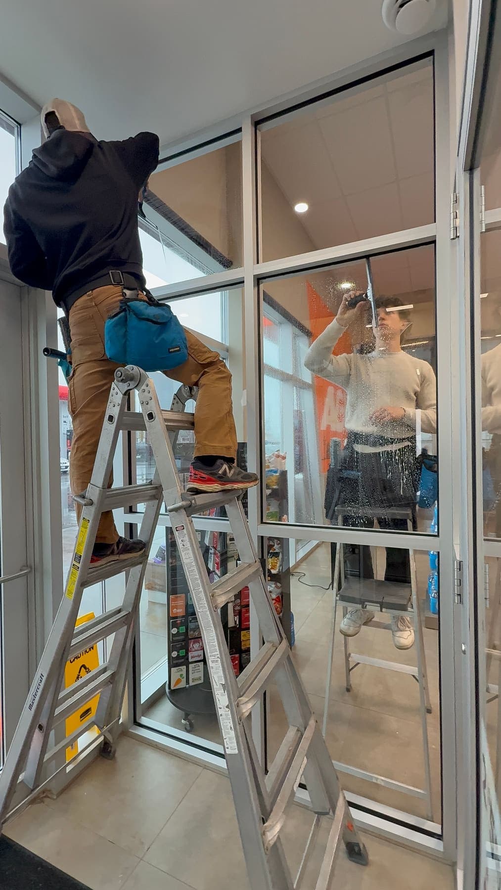 Two PVS technicians cleaning interior glass partitions on ladders