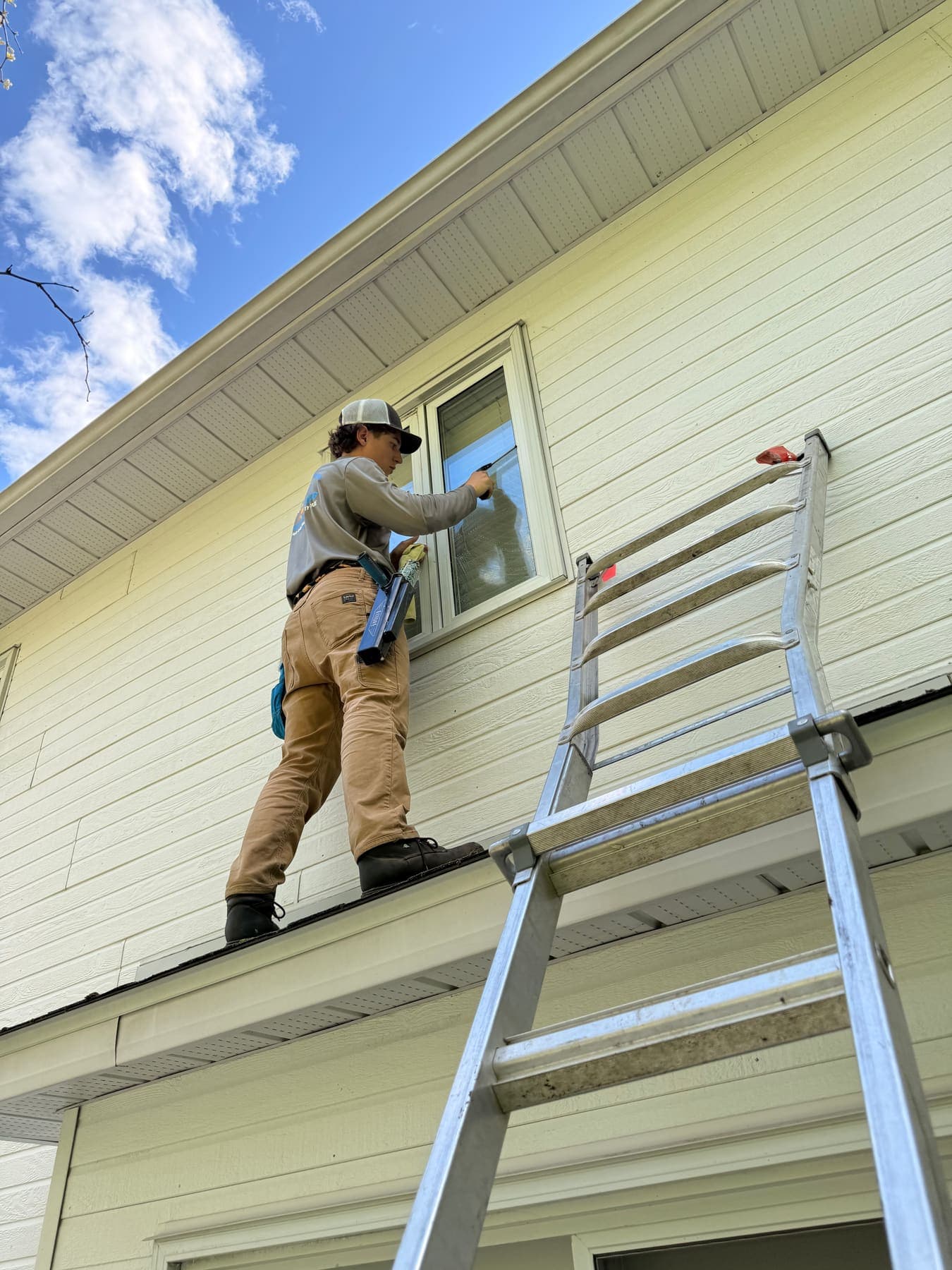 PVS technician on an extended ladder cleaning a high residential window